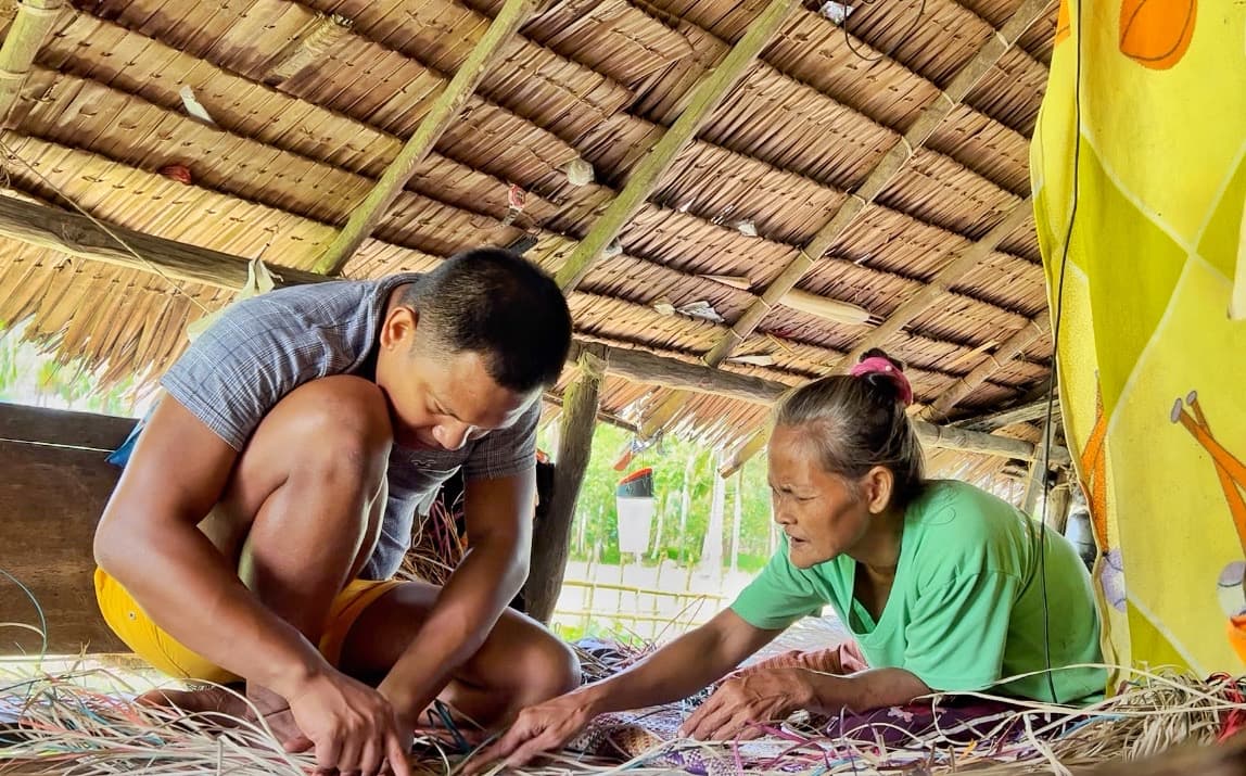 Artist Bhen Alan, bent over his work, learns about weaving from Norbena.