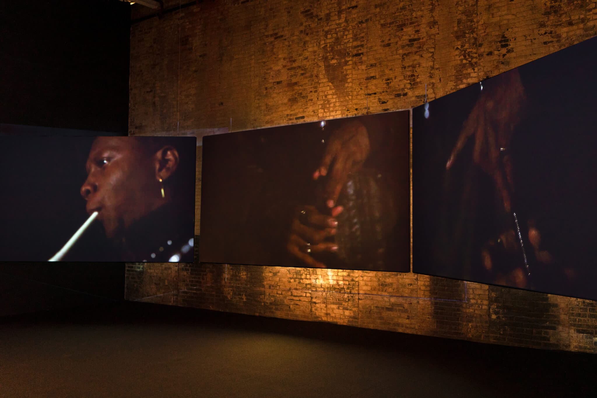 In a room with a brick wall, videos are projected, featuring the face and hands of a figure.